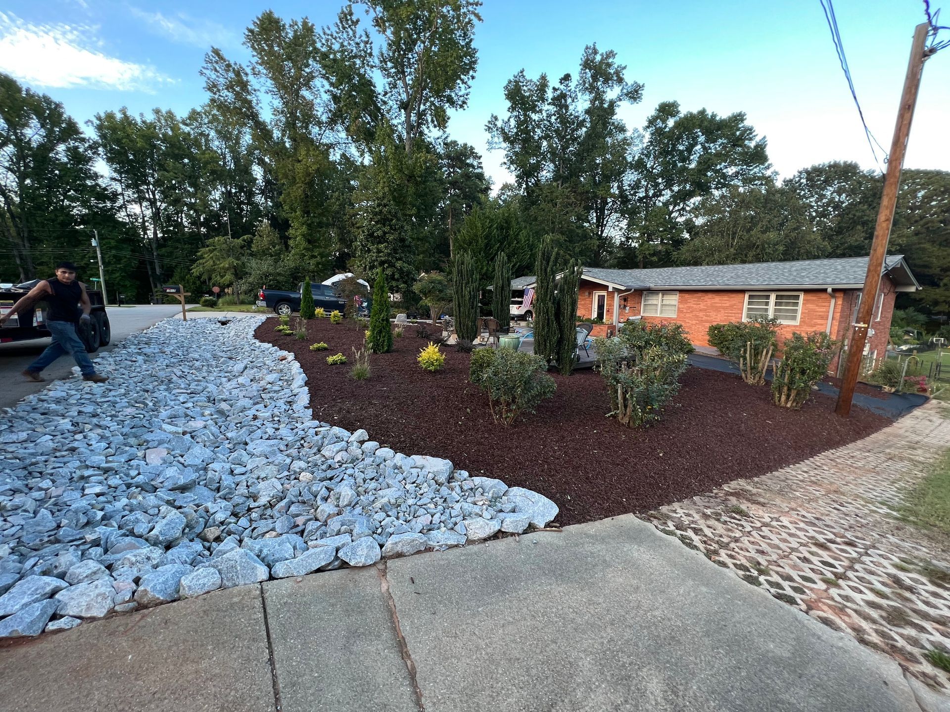 Landscaped courtyard with white rocks, red mulch, trees, and a brick building beside a paved path