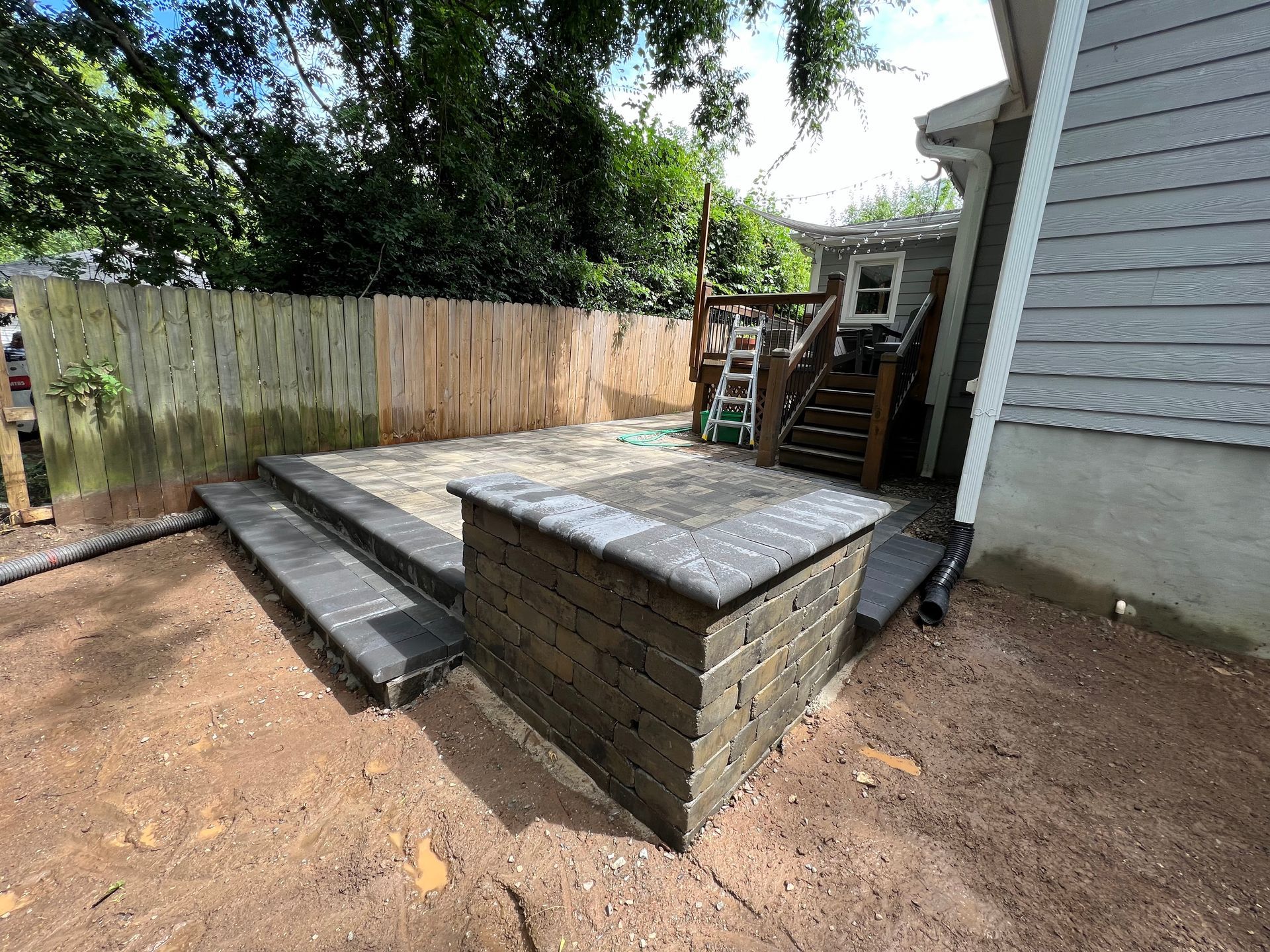 Backyard with raised wooden deck and steps, bordered by a fence and house wall.
