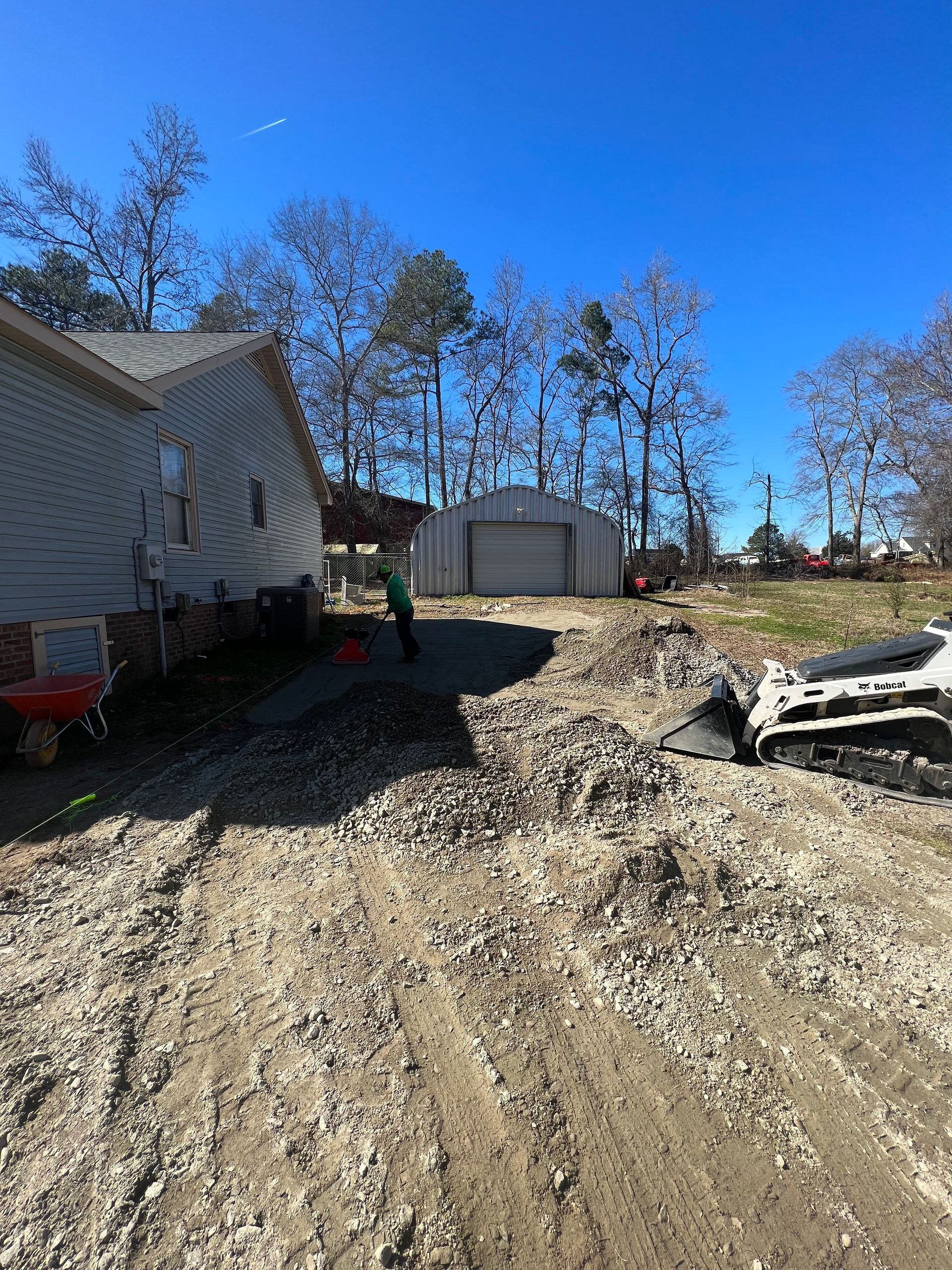 Rural gravel driveway beside a house, leading to a shed under a clear blue sky.