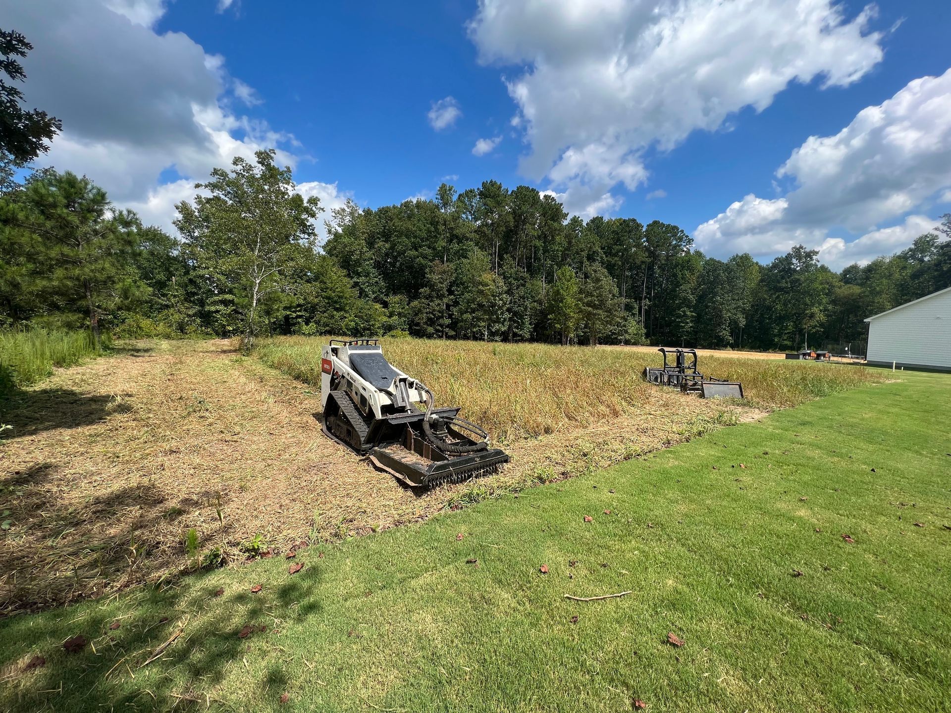 Two damaged lawn mowers in a grassy field under a blue sky with trees in the background