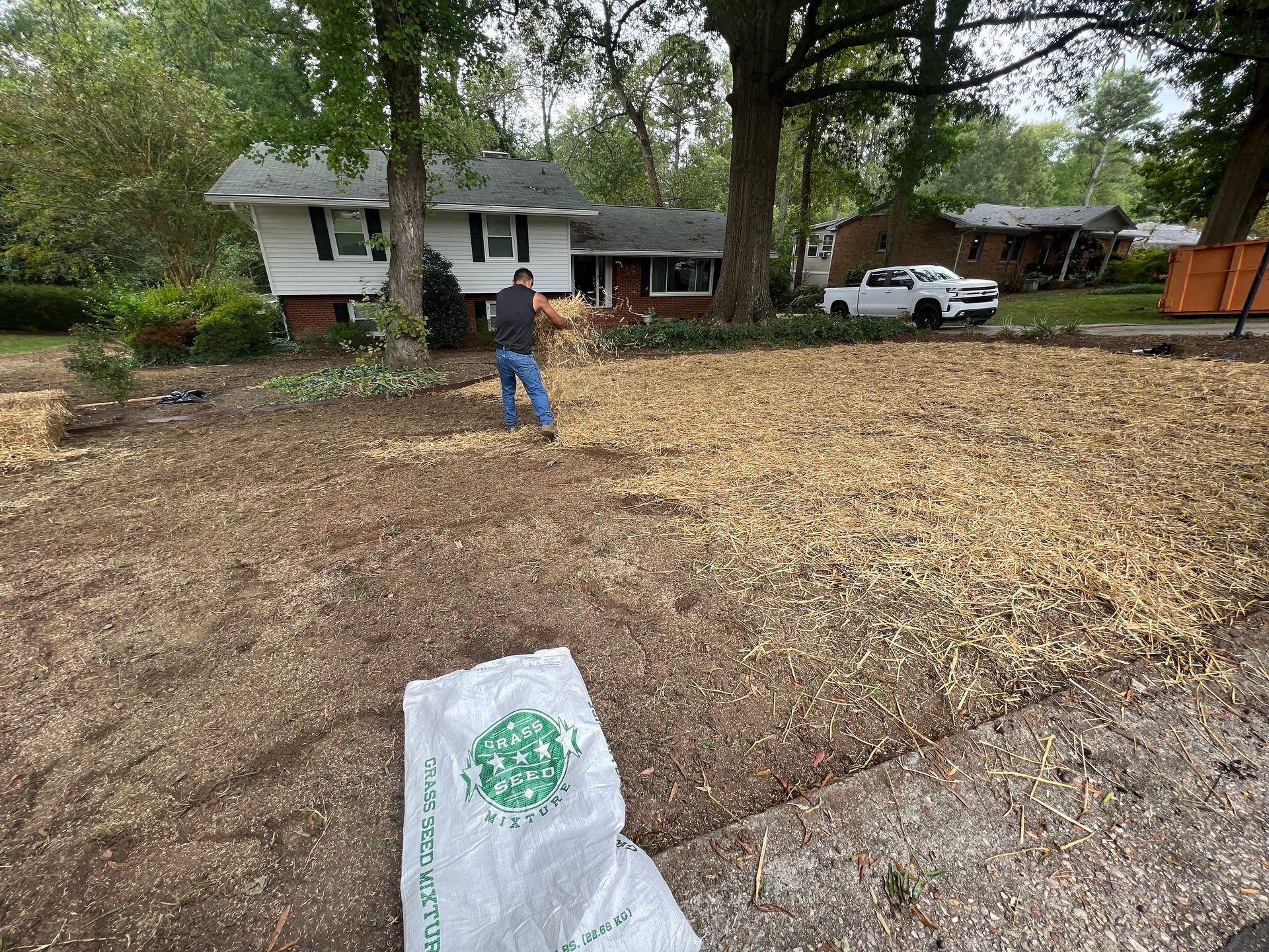 Person standing in a leaf-covered yard near a house and parked white truck.