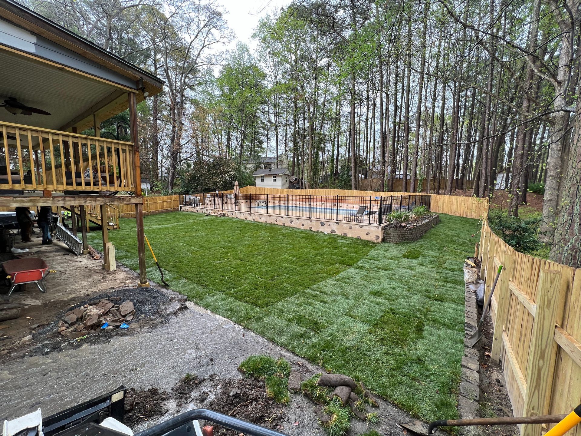 Backyard with fenced grassy yard, raised garden bed, and wooden deck beside a wooded area