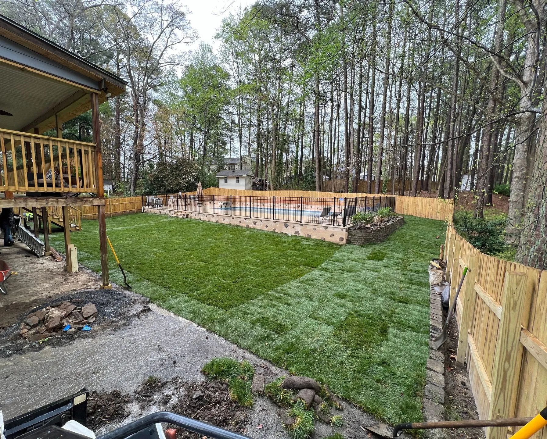 Backyard with new green lawn, fenced deck, and wooded tree line