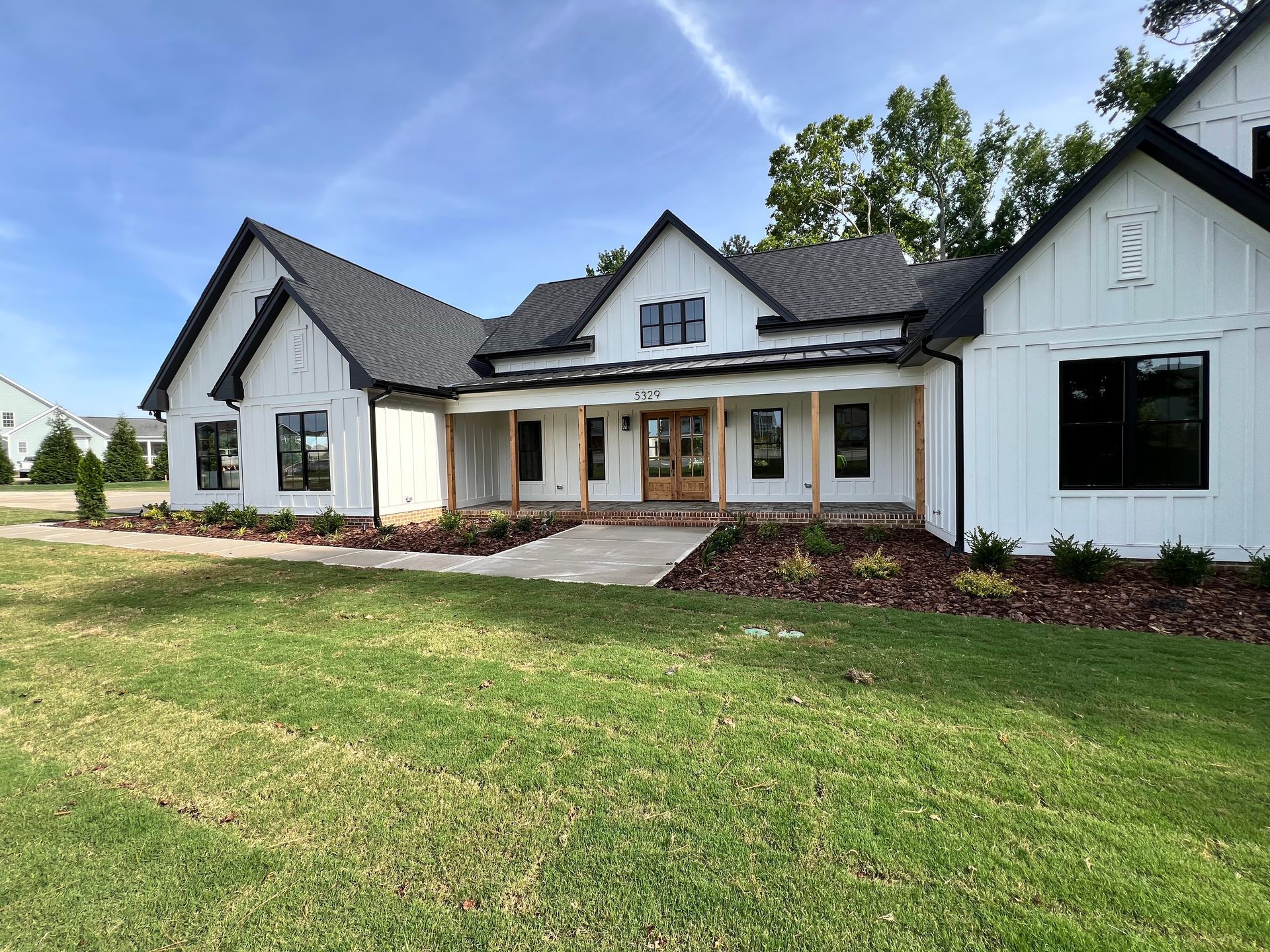 Modern white house with dark roof, front porch, and large lawn under a blue sky