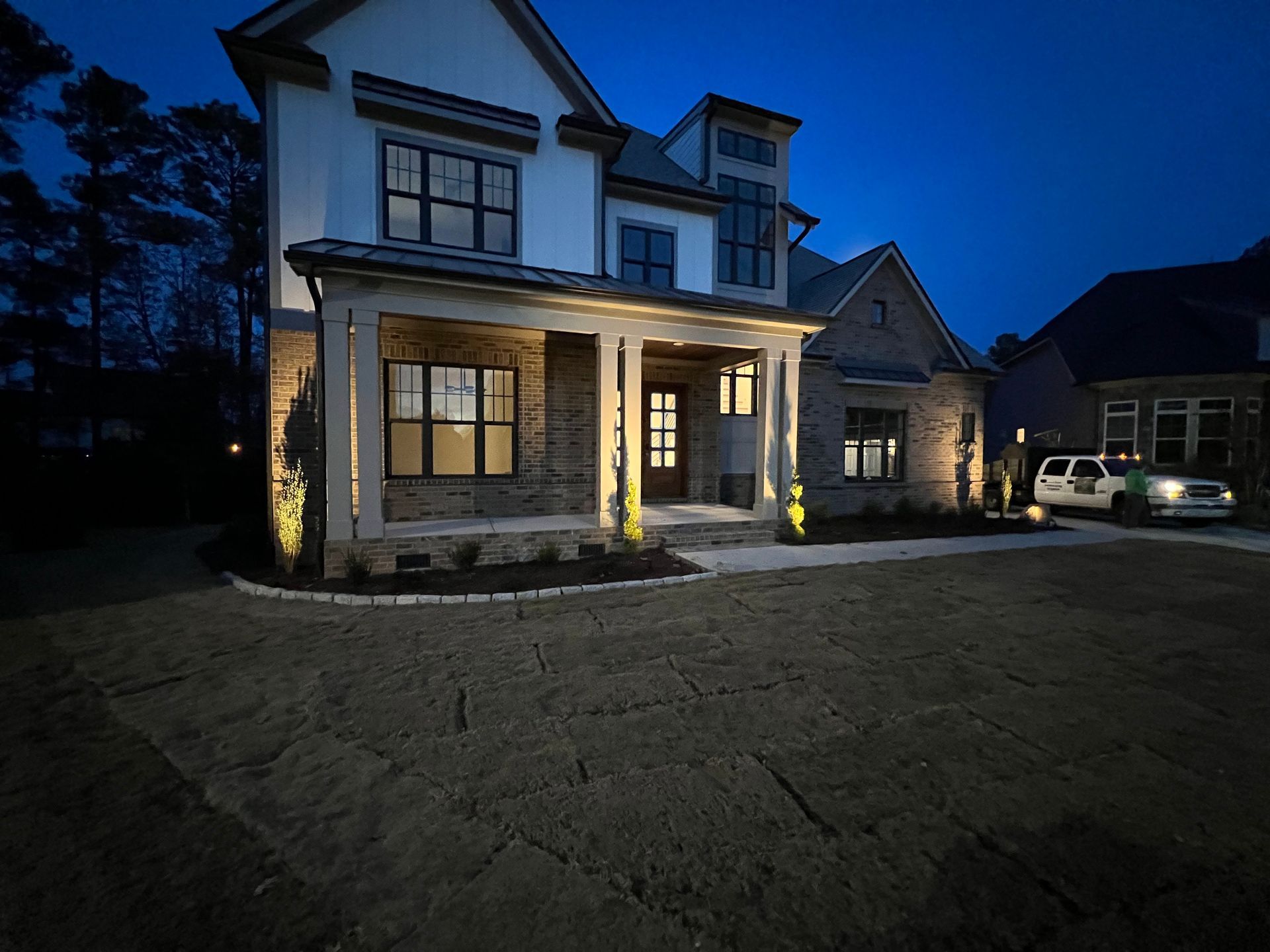 Large two-story house at dusk with lit porch and exterior lights, front lawn in foreground