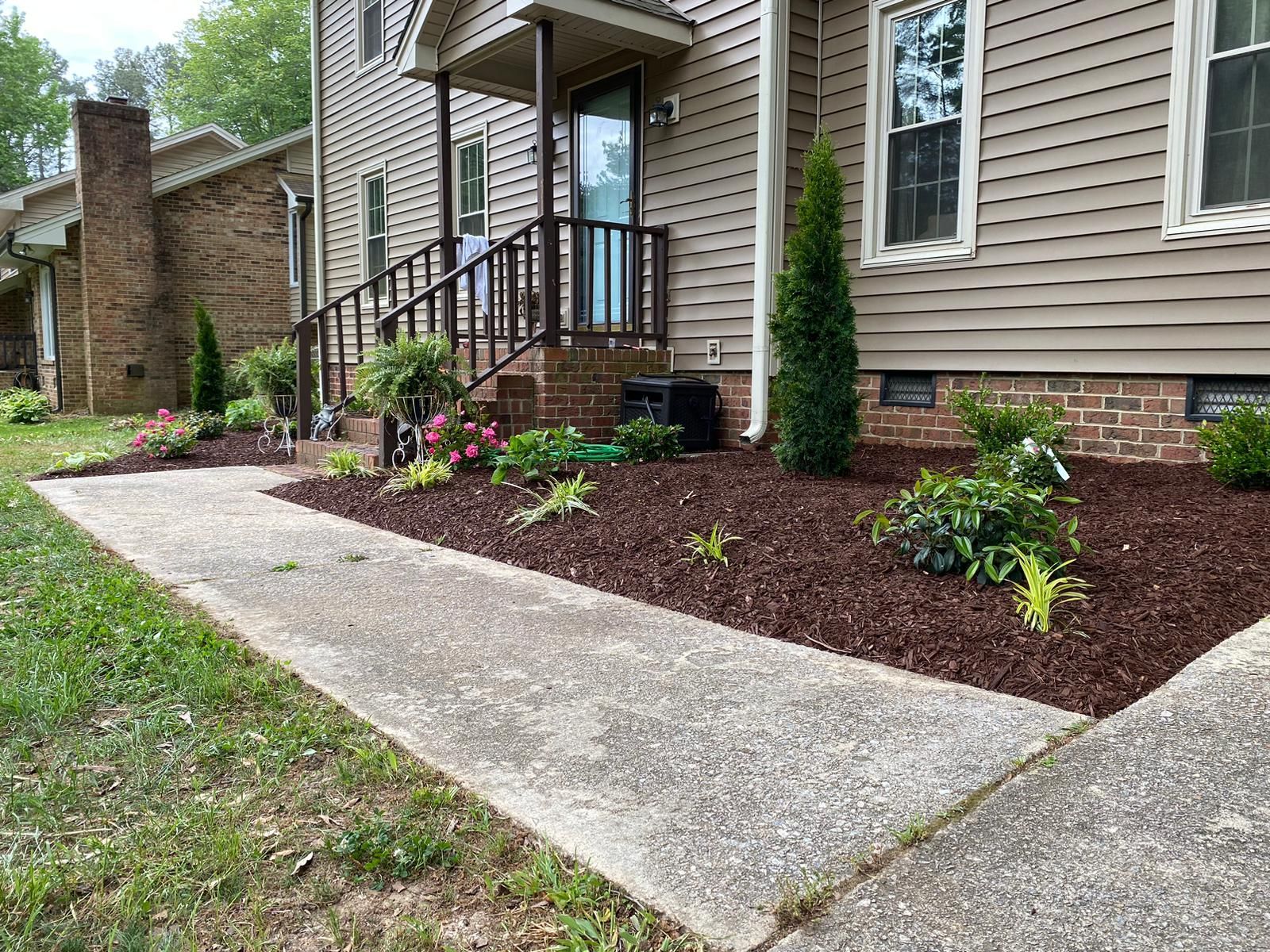 Front entry walkway with concrete path, porch steps, and newly mulched landscaping beds