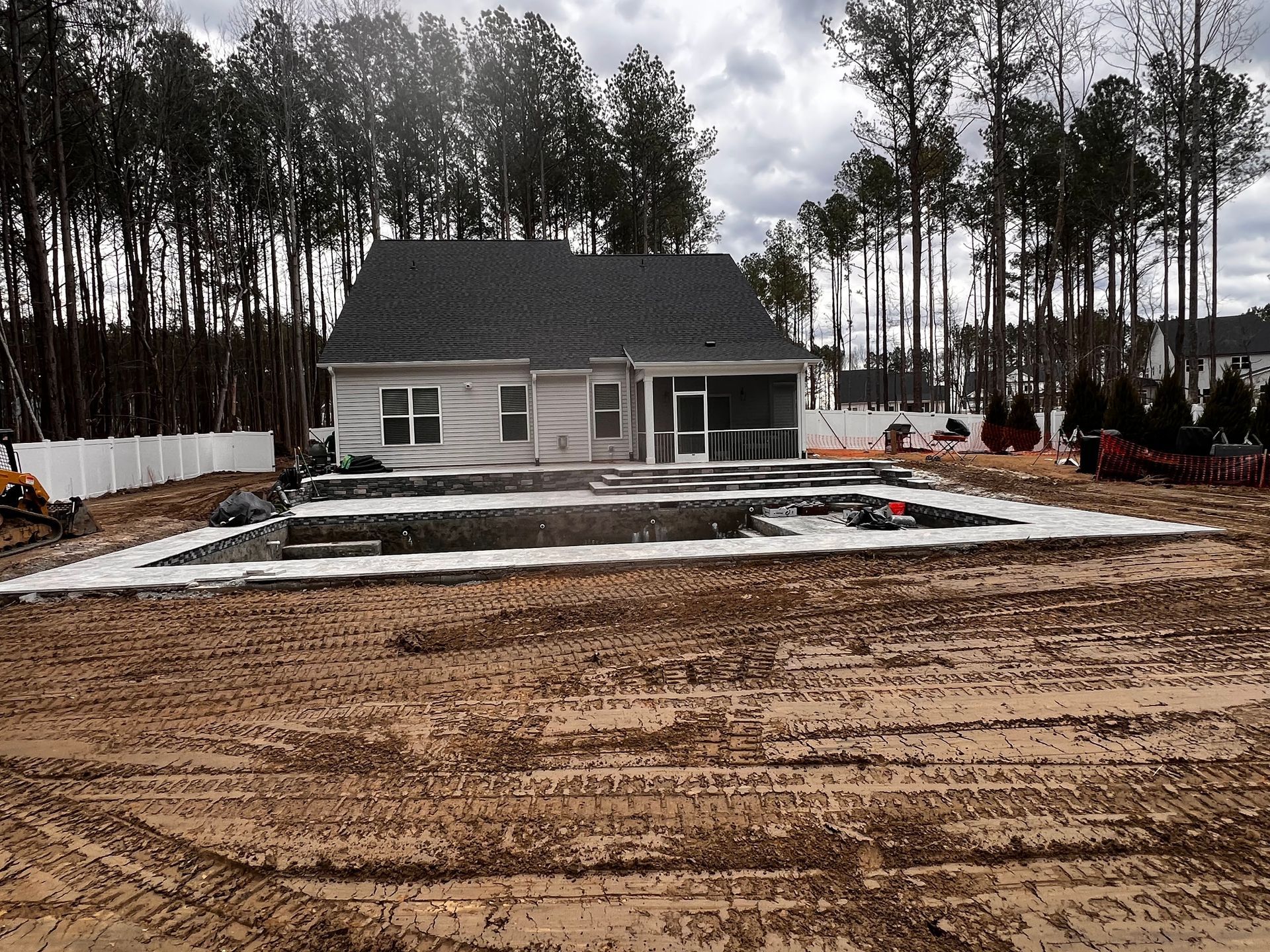 New house under construction with foundation, surrounded by trees and muddy ground