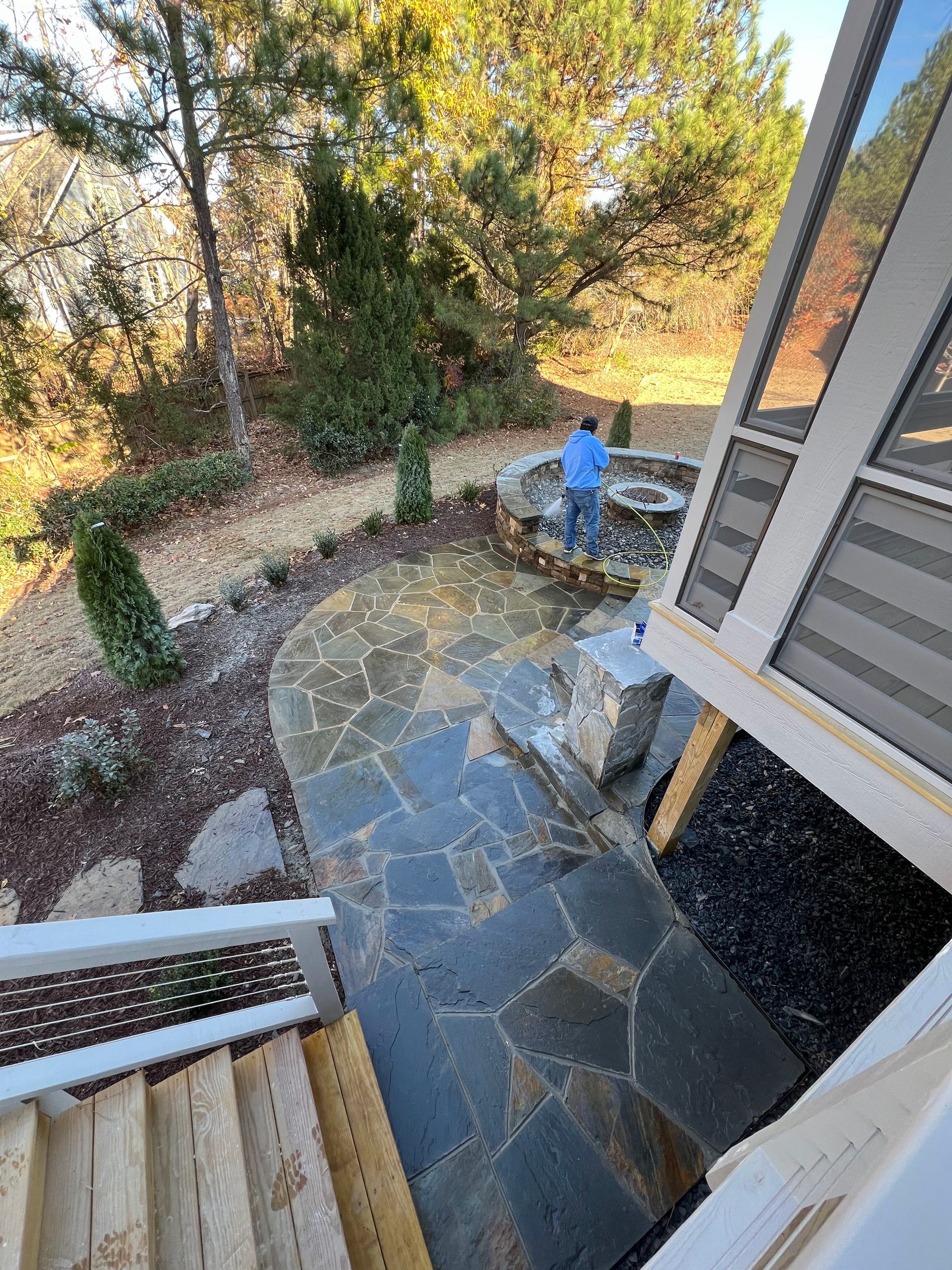 Stone patio beside house and garden, with a person standing near a circular fire pit.