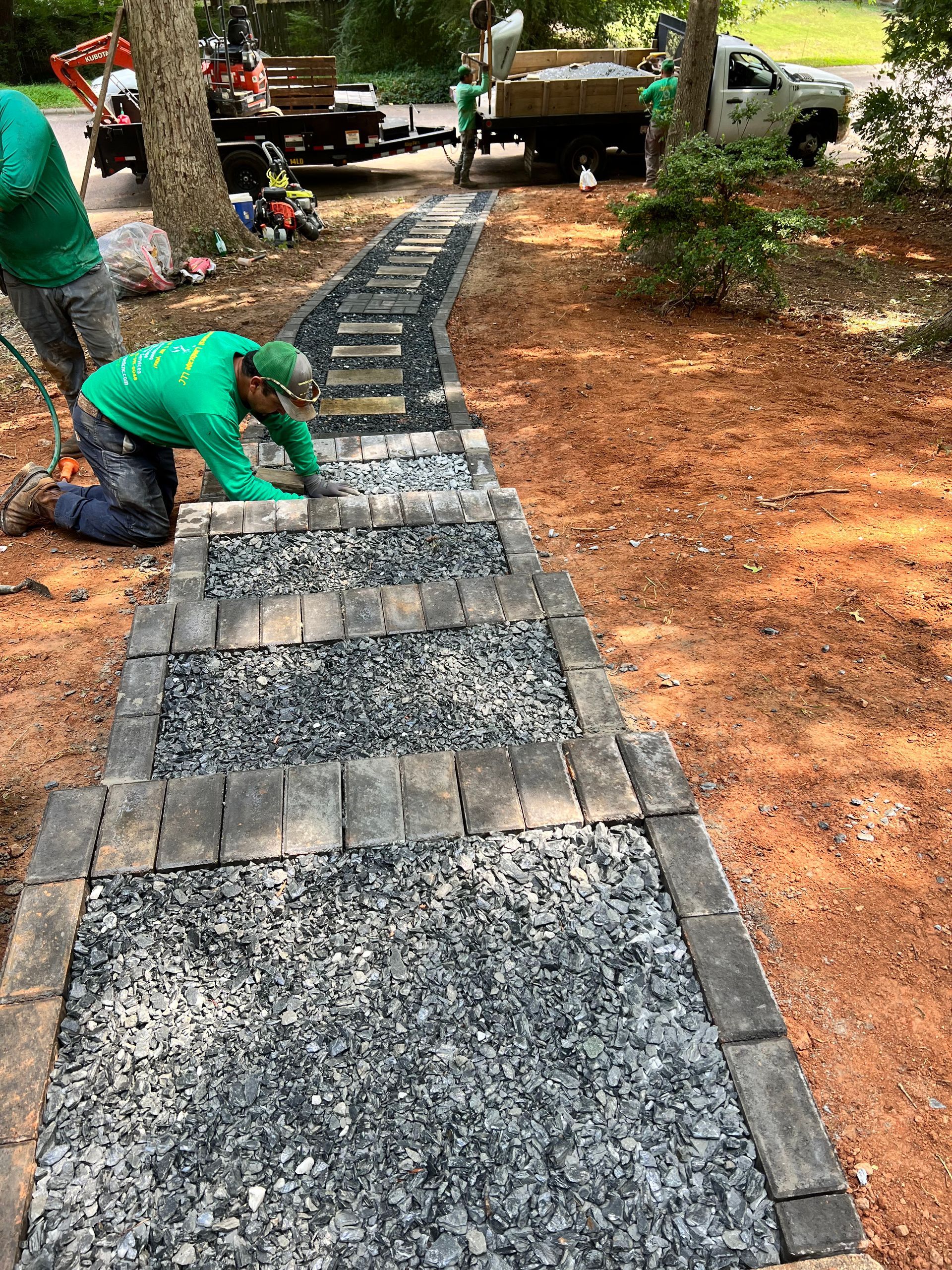 Worker in green shirt laying stone pavers for a garden walkway with curved edge.