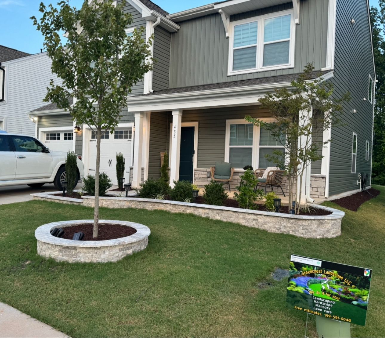 Two-story gray house with a small front porch, lawn, young tree, and a white van in the driveway.