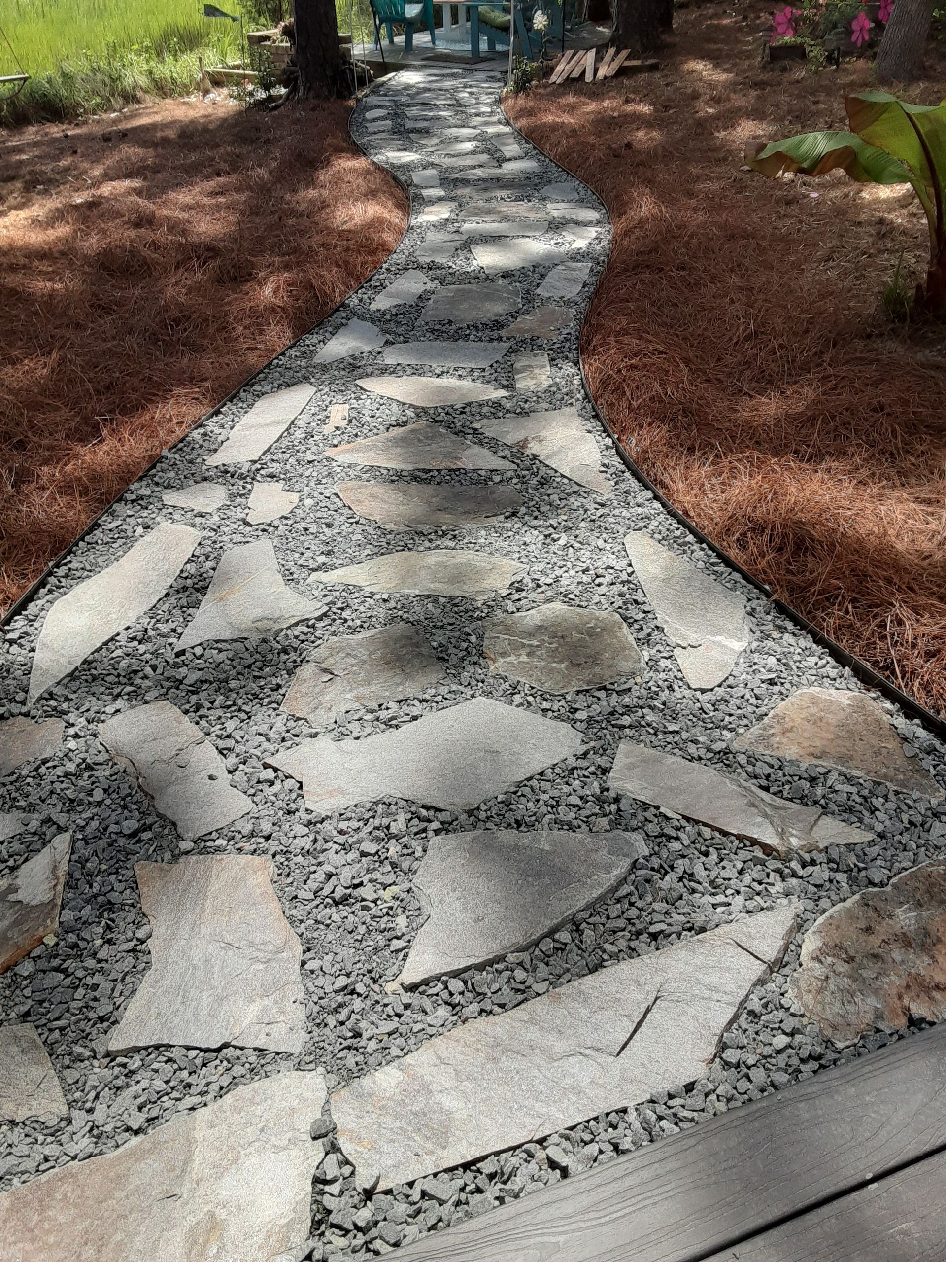 Curved mosaic stone walkway bordered by red mulch in a garden setting