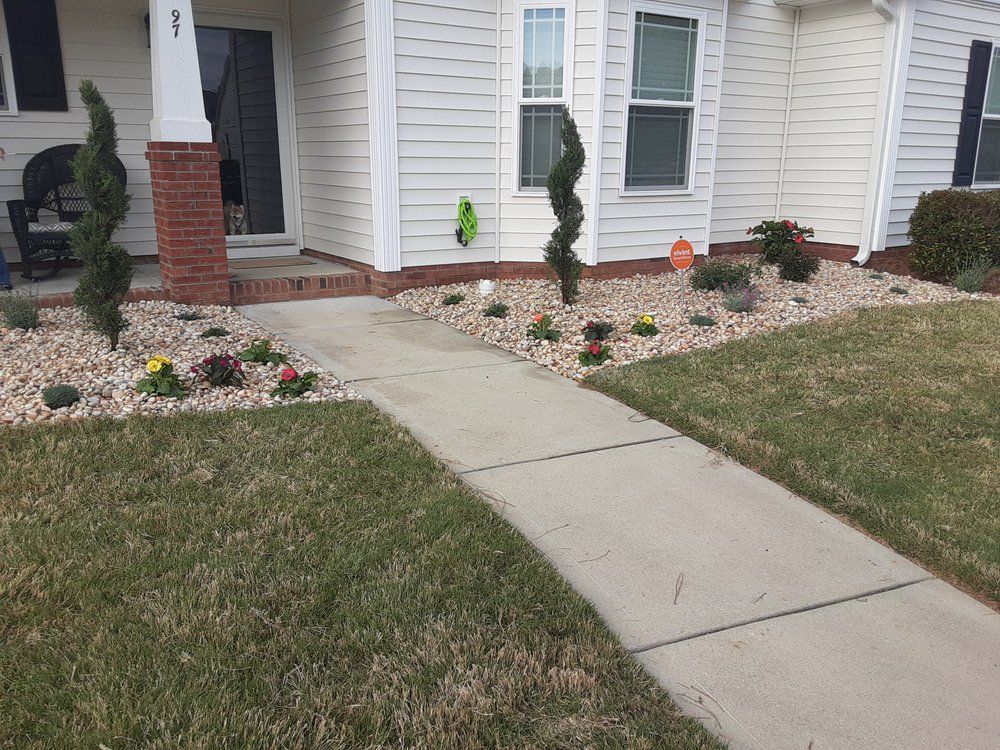 Curved stone walkway around a landscaped front yard with a truck and red excavator in the background