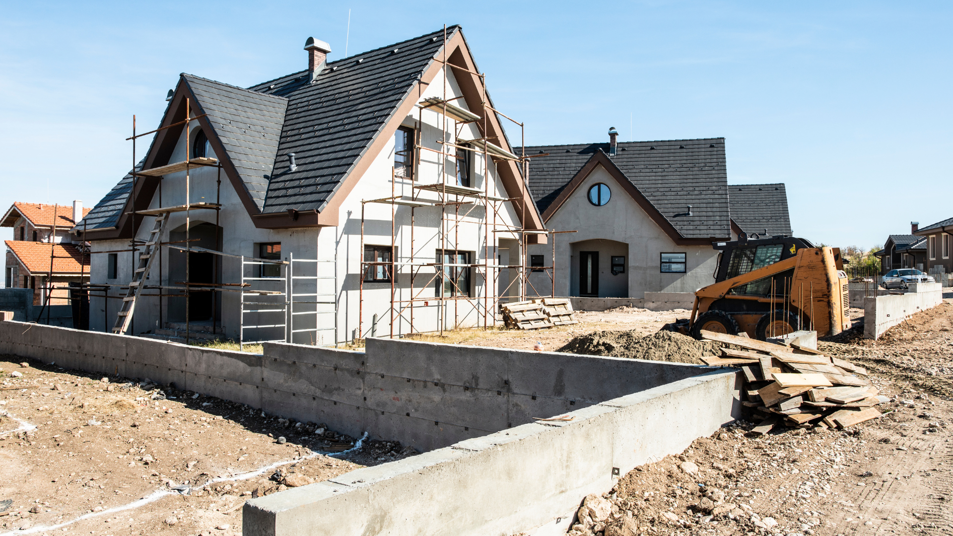 A house is being built in a residential area with a bulldozer in the background.
