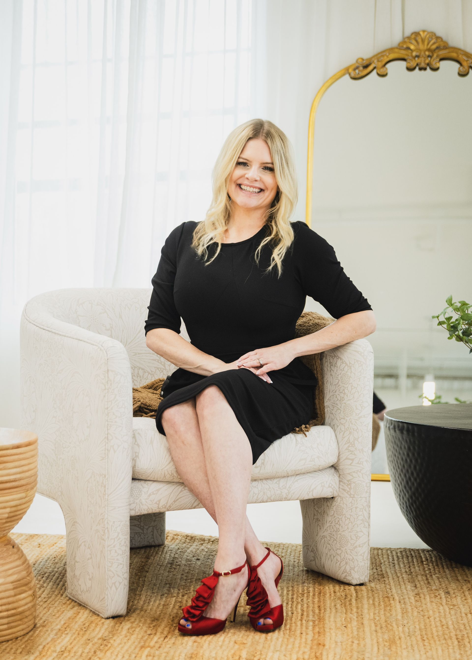 A woman in a black dress is leaning on a couch.