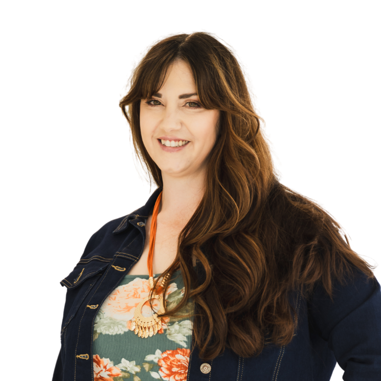 A woman wearing a floral shirt and a denim jacket smiles for the camera