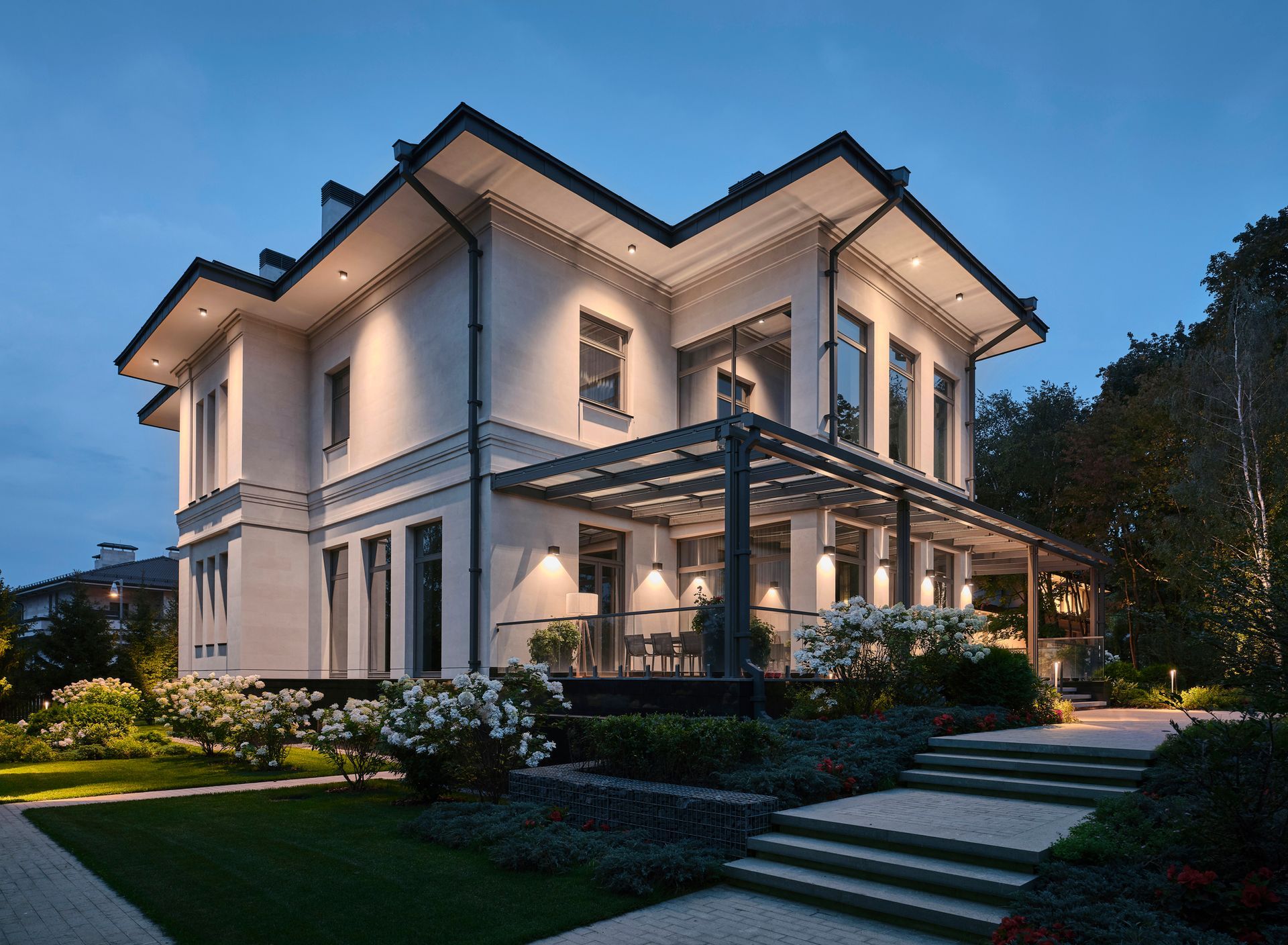 A large white house with a large porch and stairs is lit up at night.