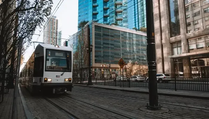 A trolley is driving down a city street next to a tall building.