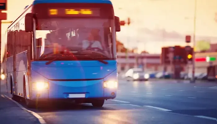 A blue bus is driving down a city street at sunset.