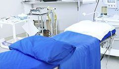 A hospital bed with a blue blanket and a white pillow.