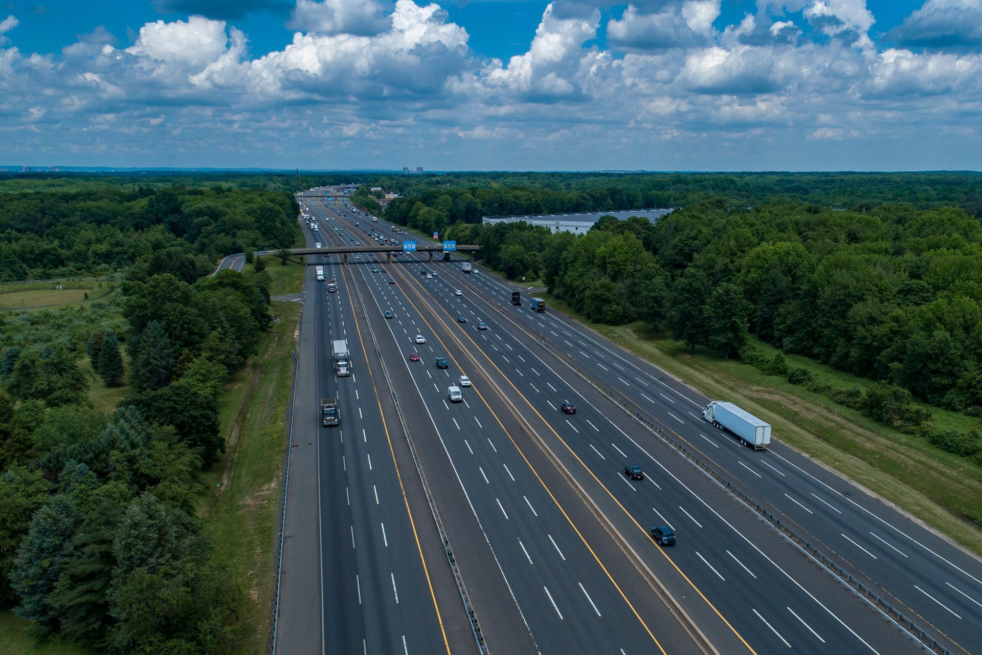 An aerial view of a highway surrounded by trees on a sunny day.