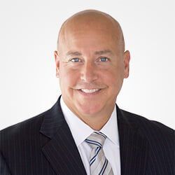 A bald man in a suit and tie is smiling for the camera.