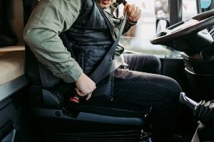A man is sitting in the driver 's seat of a truck and putting on his seat belt.
