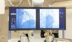 Two monitors are hanging from the ceiling in a hospital room.