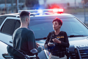 A woman is talking to a man in front of a police car.