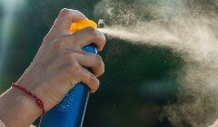 A person is spraying sunscreen on their face.