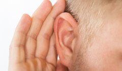 A man is holding his hand to his ear to hear something.