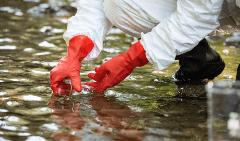 A person wearing red gloves is kneeling in a puddle of water.