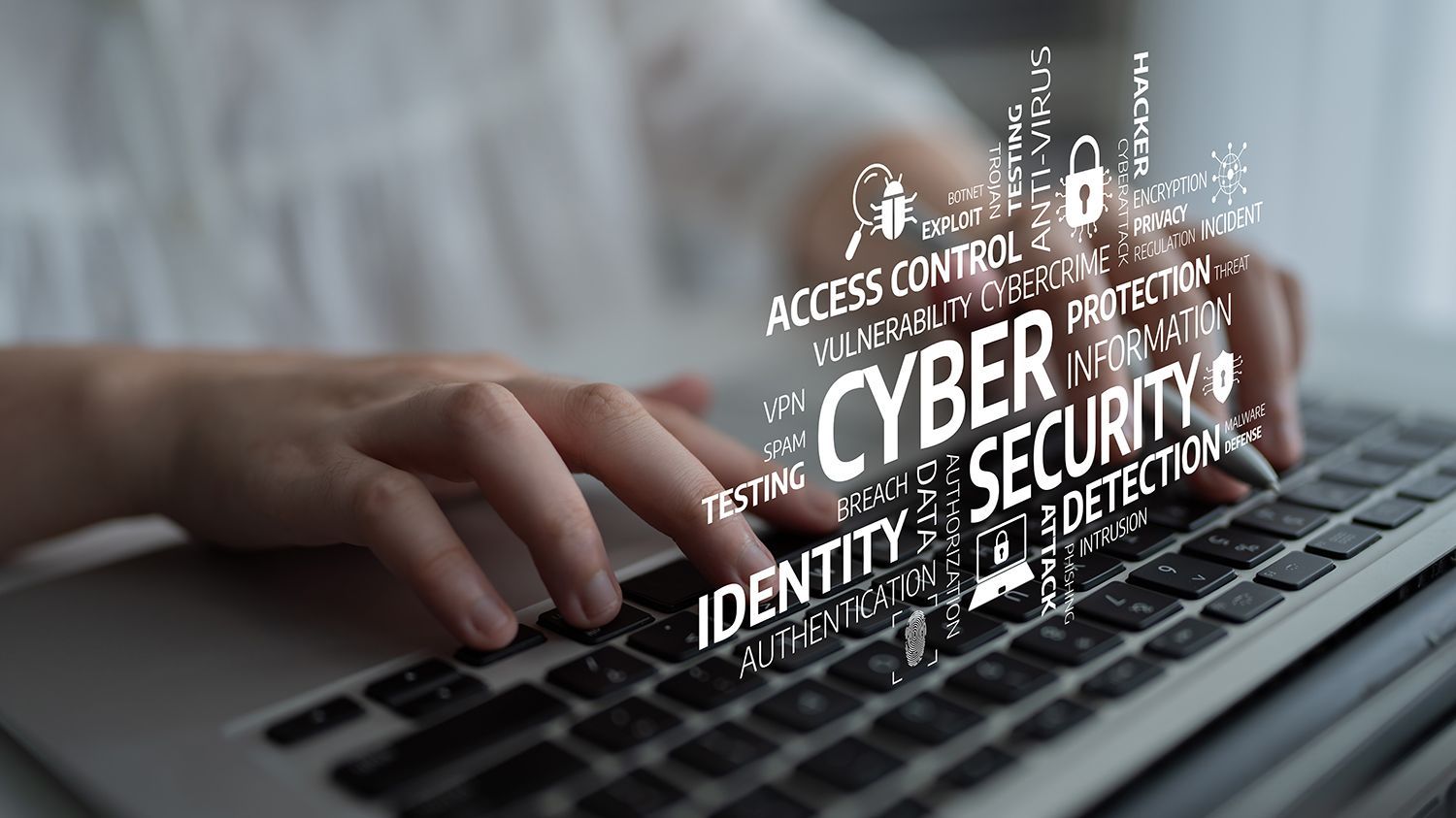 Hands typing on a laptop with cybersecurity keywords overlayed across the keyboard. Hands typing on a laptop with cybersecurity keywords overlayed across the keyboard.