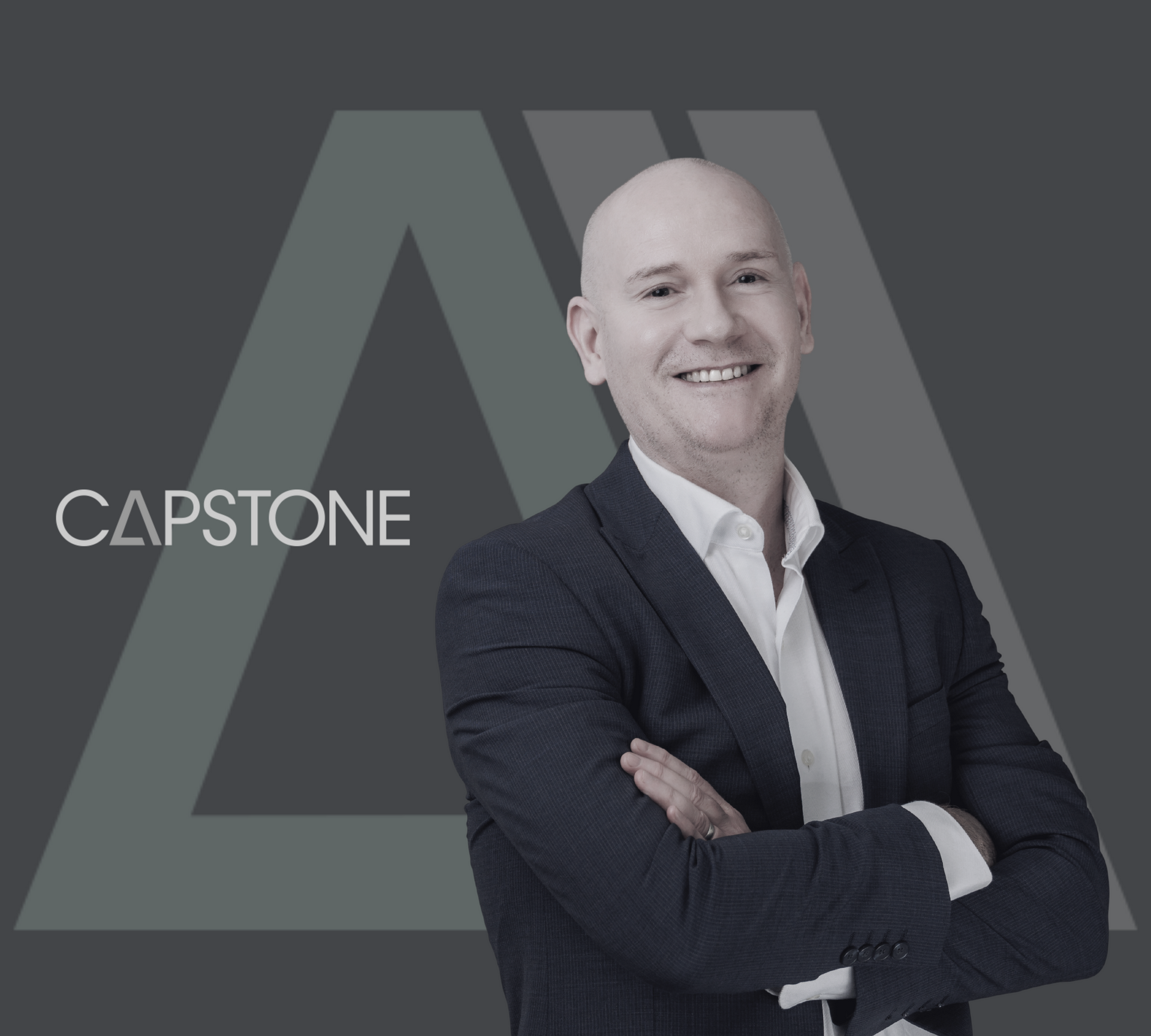 Smiling bald man in suit with crossed arms, Capstone logo in background.