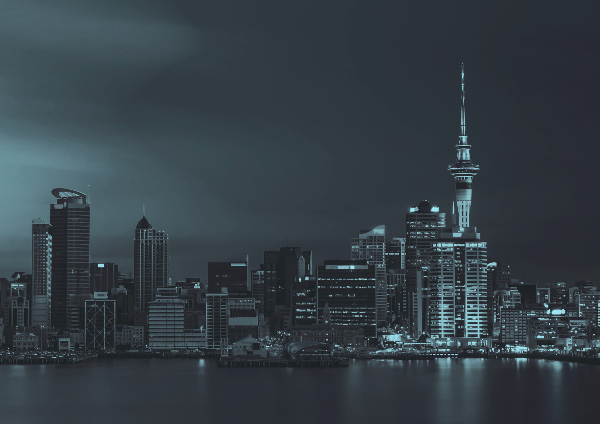 Night view of Auckland city skyline, including the Sky Tower, in shades of teal.