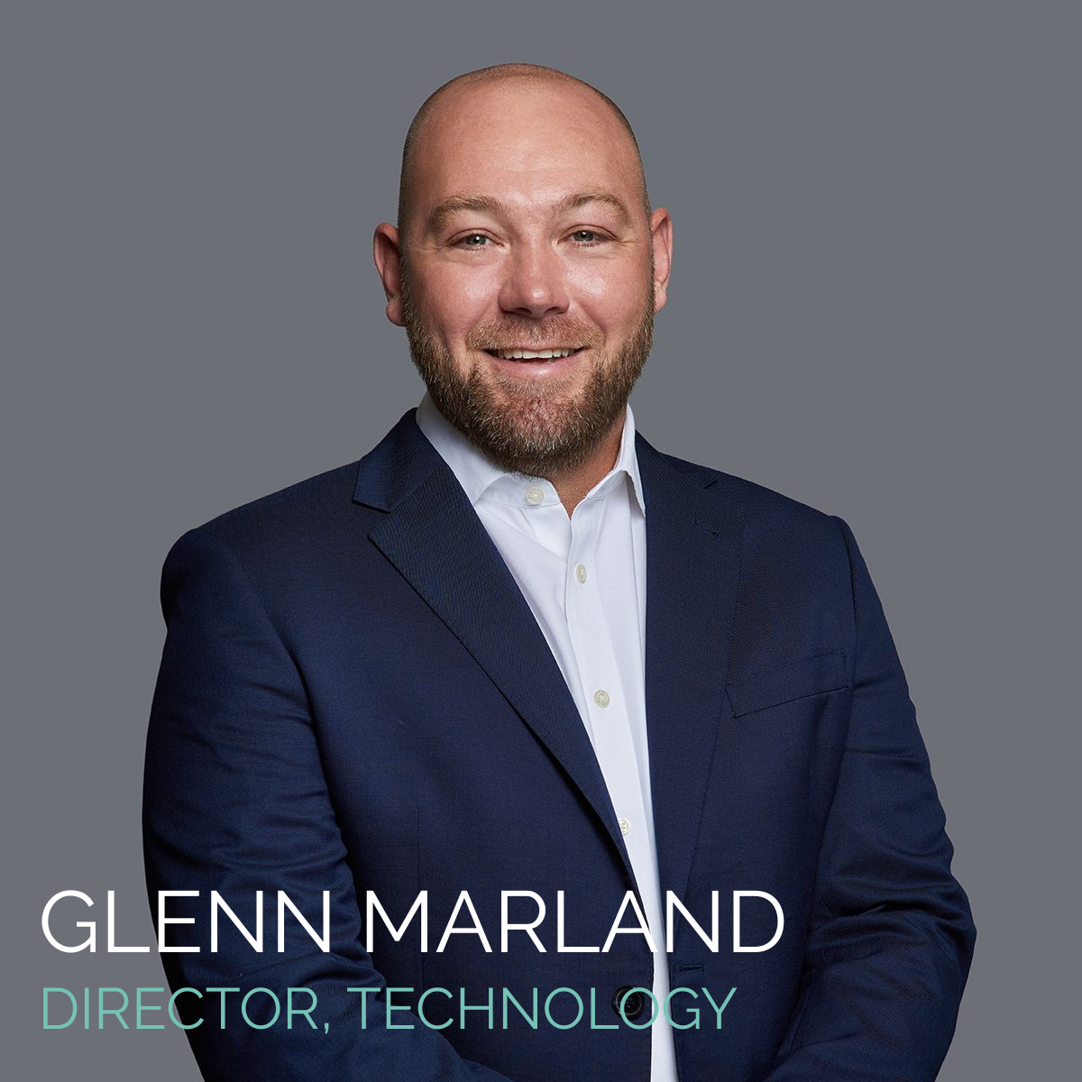 Glenn Marland, Director of Technology, smiling. Wearing a navy blue suit and a white shirt. Gray background.