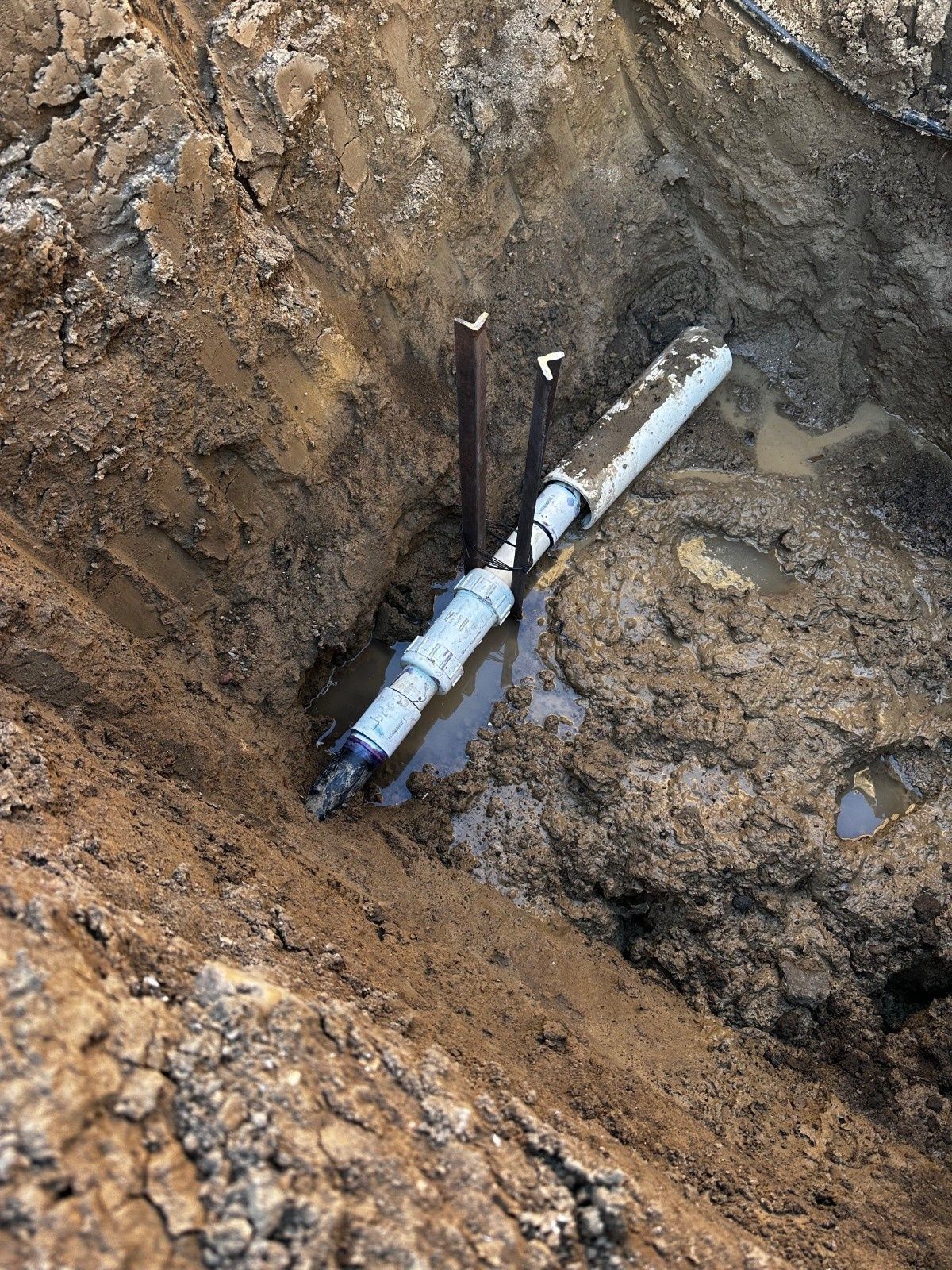 A newly installed pipe section with a coupling fitting located inside a muddy, open trench.