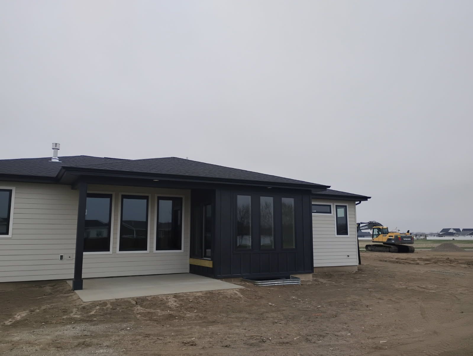 Single-story house with black trim and light siding under construction on a bare lot.