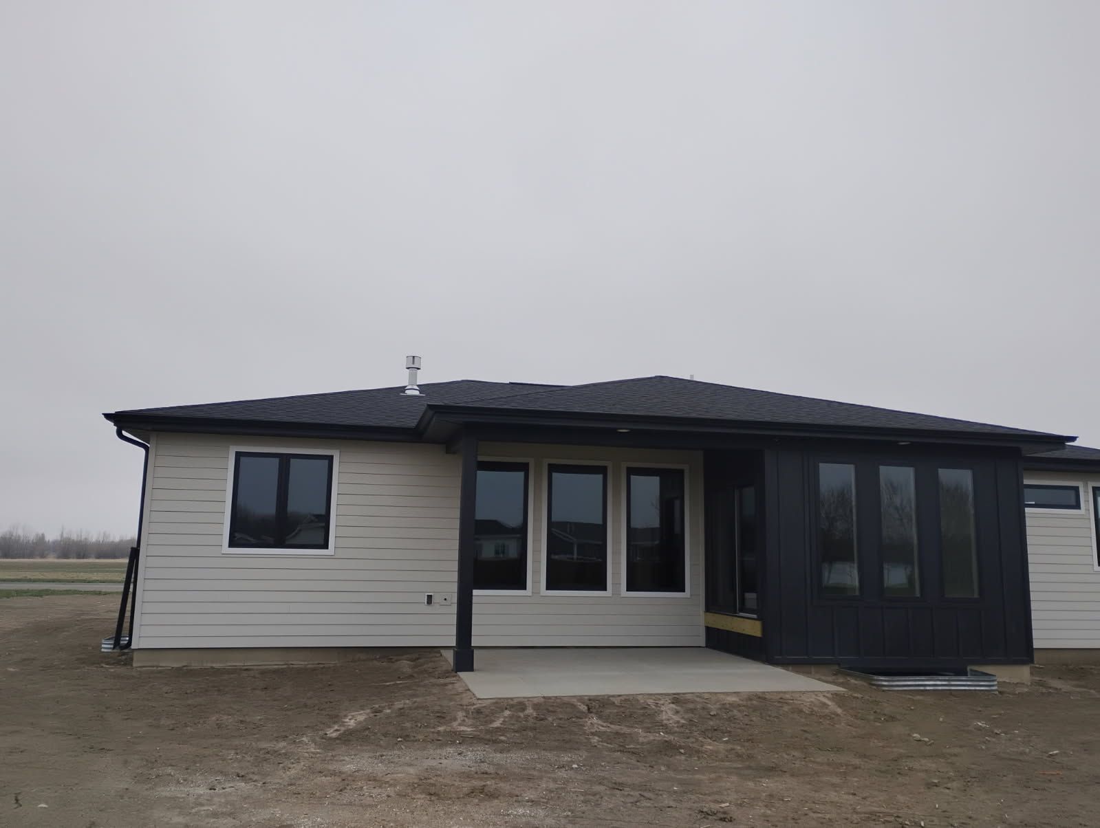 Small single-story house with beige siding and dark-trimmed windows under an overcast sky.