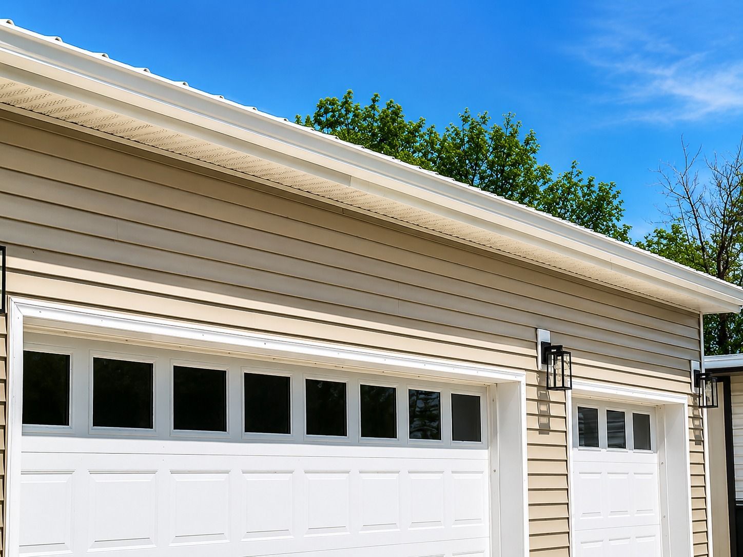 White garage doors on a beige house with tan siding and blue sky overhead