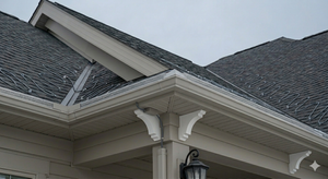 House roofline and porch eaves with gray shingles and white trim under an overcast sky
