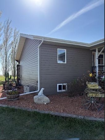 Side view of a tan house with a small window and landscaped yard under a blue sky.