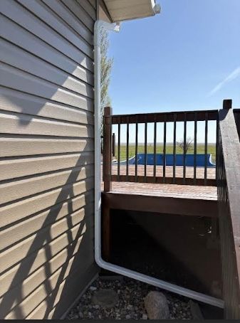 Side yard stairway beside beige siding, with wooden railing and a view of water beyond.