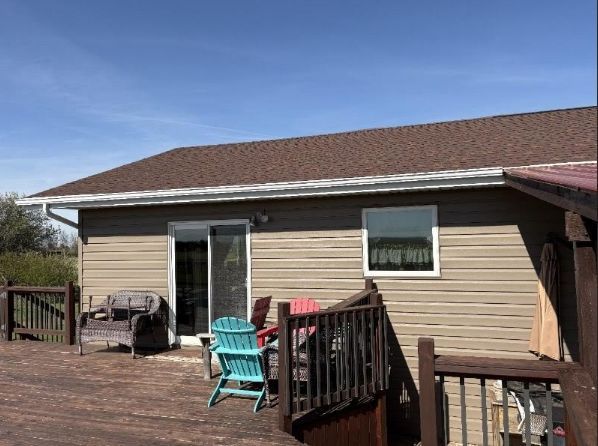 Back deck with turquoise chairs and grill against tan house under a clear blue sky