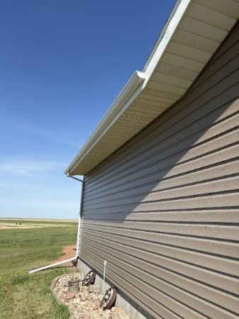 Side view of a tan house with vinyl siding under a blue sky in a grassy rural field