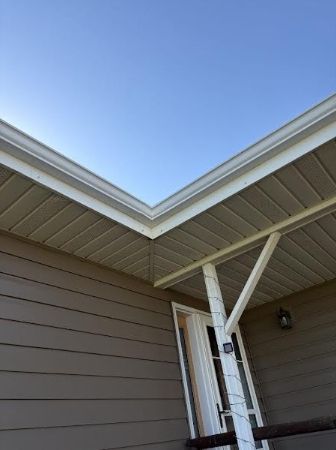 Corner of a house exterior with tan siding, white trim, and a small covered porch against a blue sky