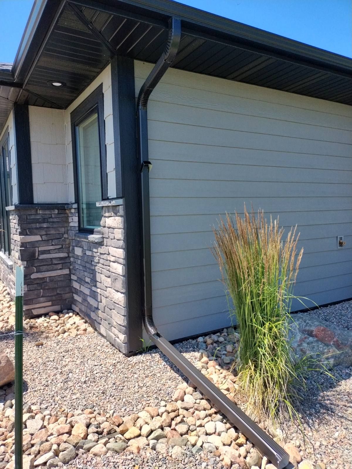 Side of a house with gray siding, stone entry wall, and gravel landscaping with a tall ornamental grass.