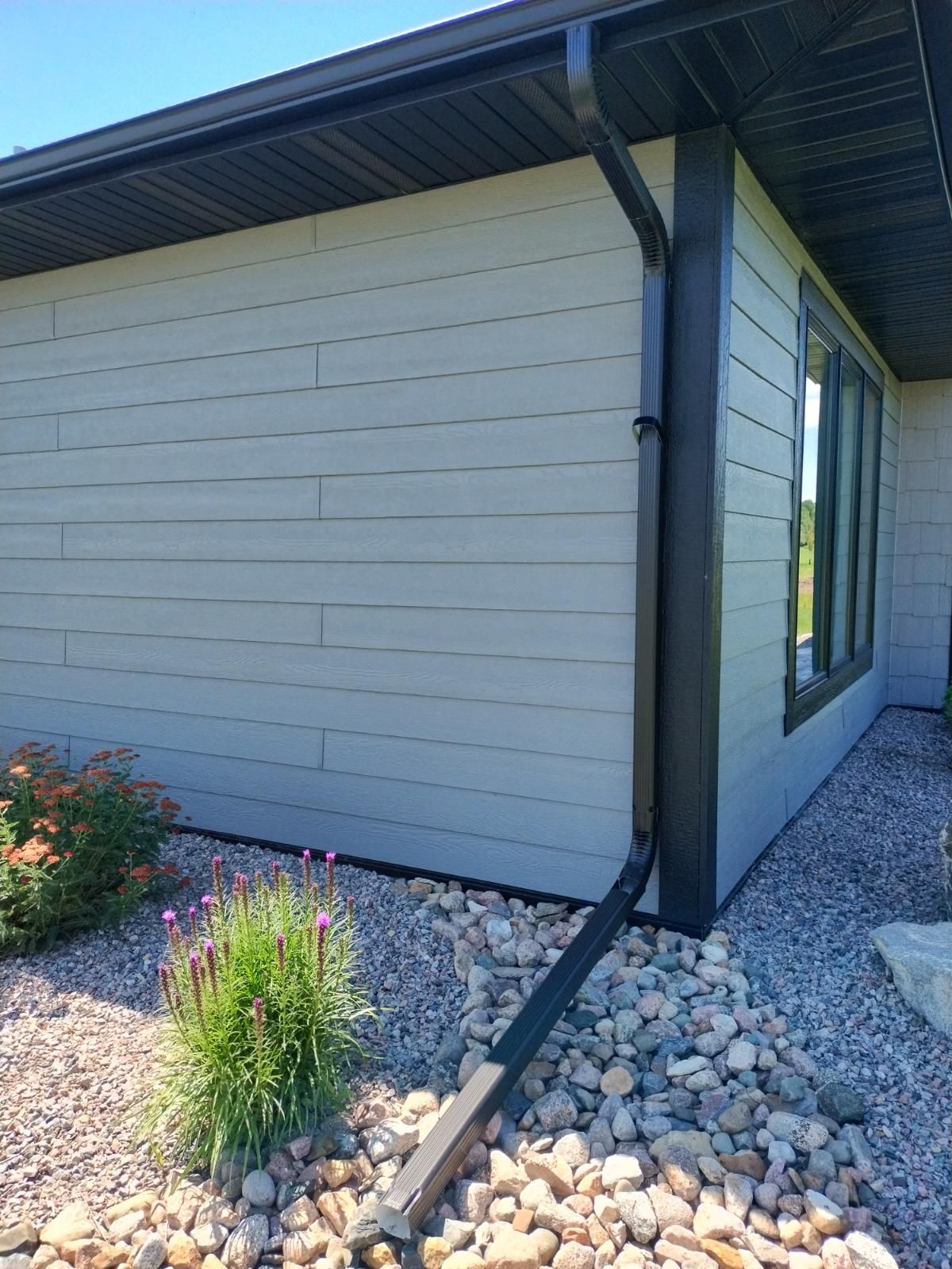Modern house exterior with white siding, black trim, gravel landscaping, and flower beds