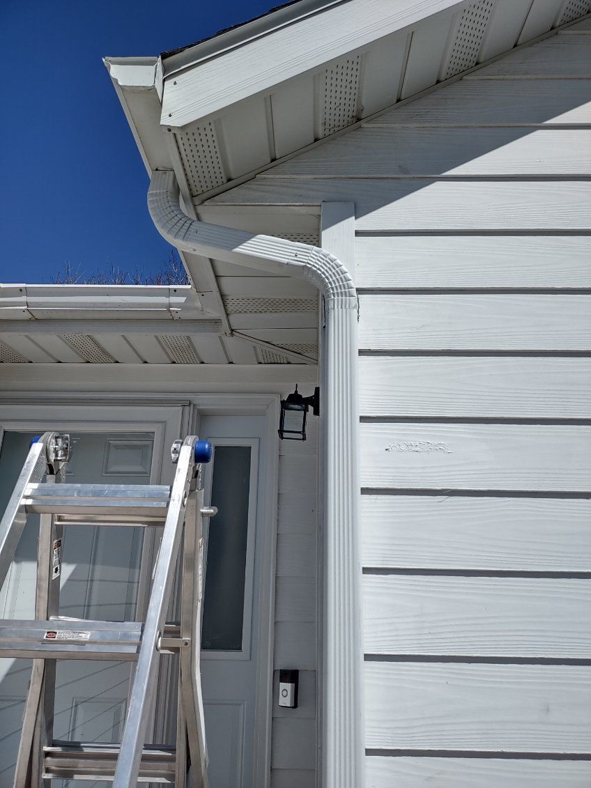 White house exterior with a ladder under the eaves and a white gutter against a blue sky