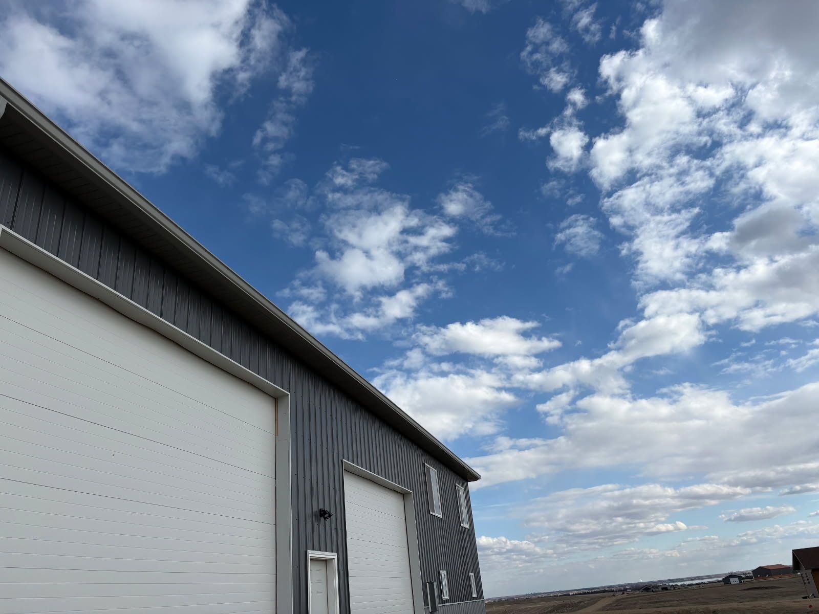 Gray metal building with a large white garage door under a partly cloudy blue sky