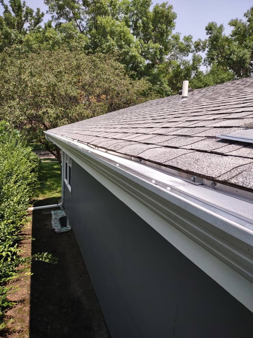 Gutter along gray shingled roof edge with trees in the background